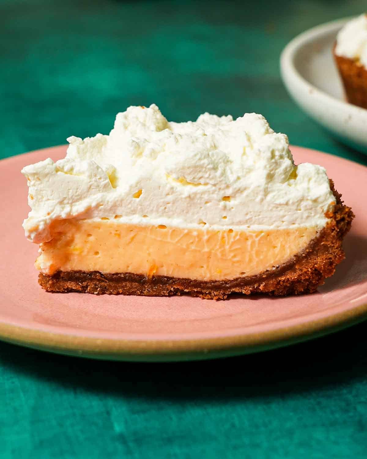 A pink plate with a Meyer lemon pie slice topped with whipped cream.