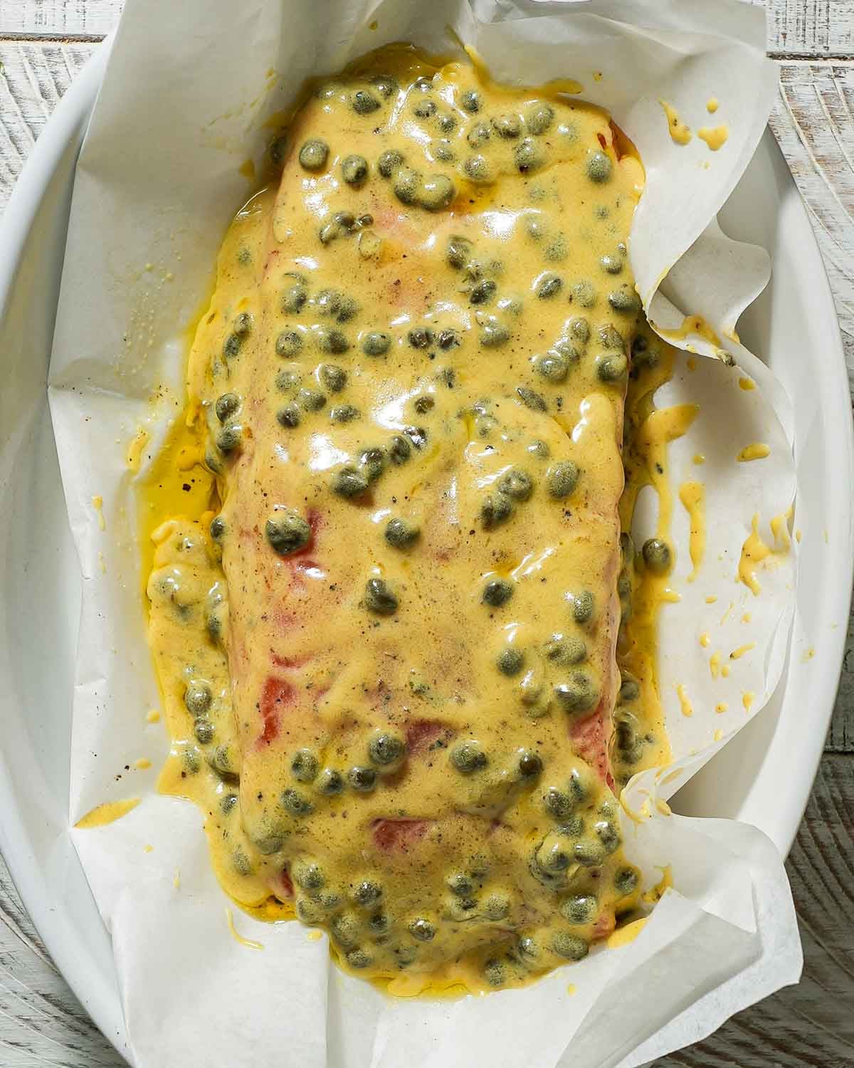Dijon mustard marinade over salmon in a baking dish before baking.
