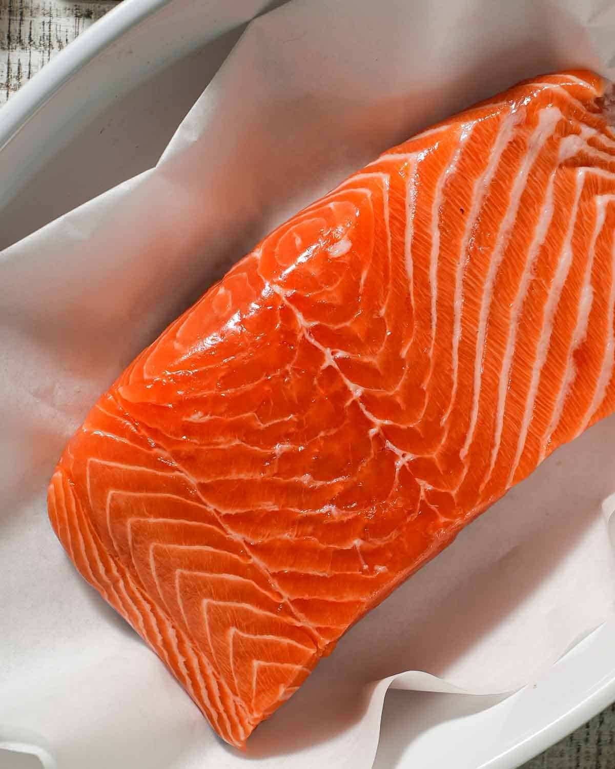 A salmon fillet in a baking dish lined with parchment paper.