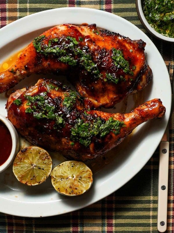 A platter of grilled honey chipotle bbq chicken with grilled limes and cilantro lime gremolata on a plaid tablecloth.