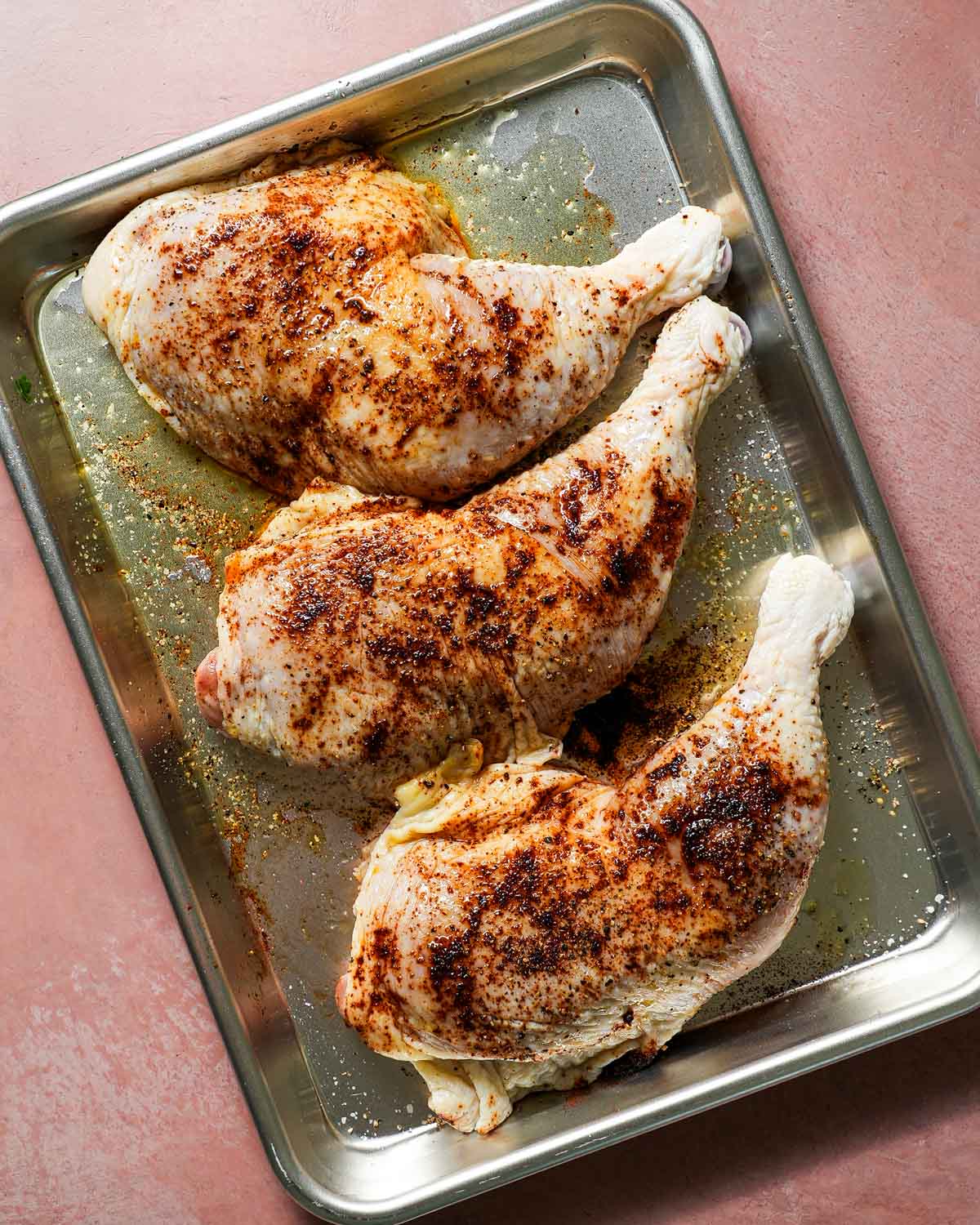 Raw chicken on a baking sheet with chipotle powder, salt, pepper, and olive oil ready to go on the grill.