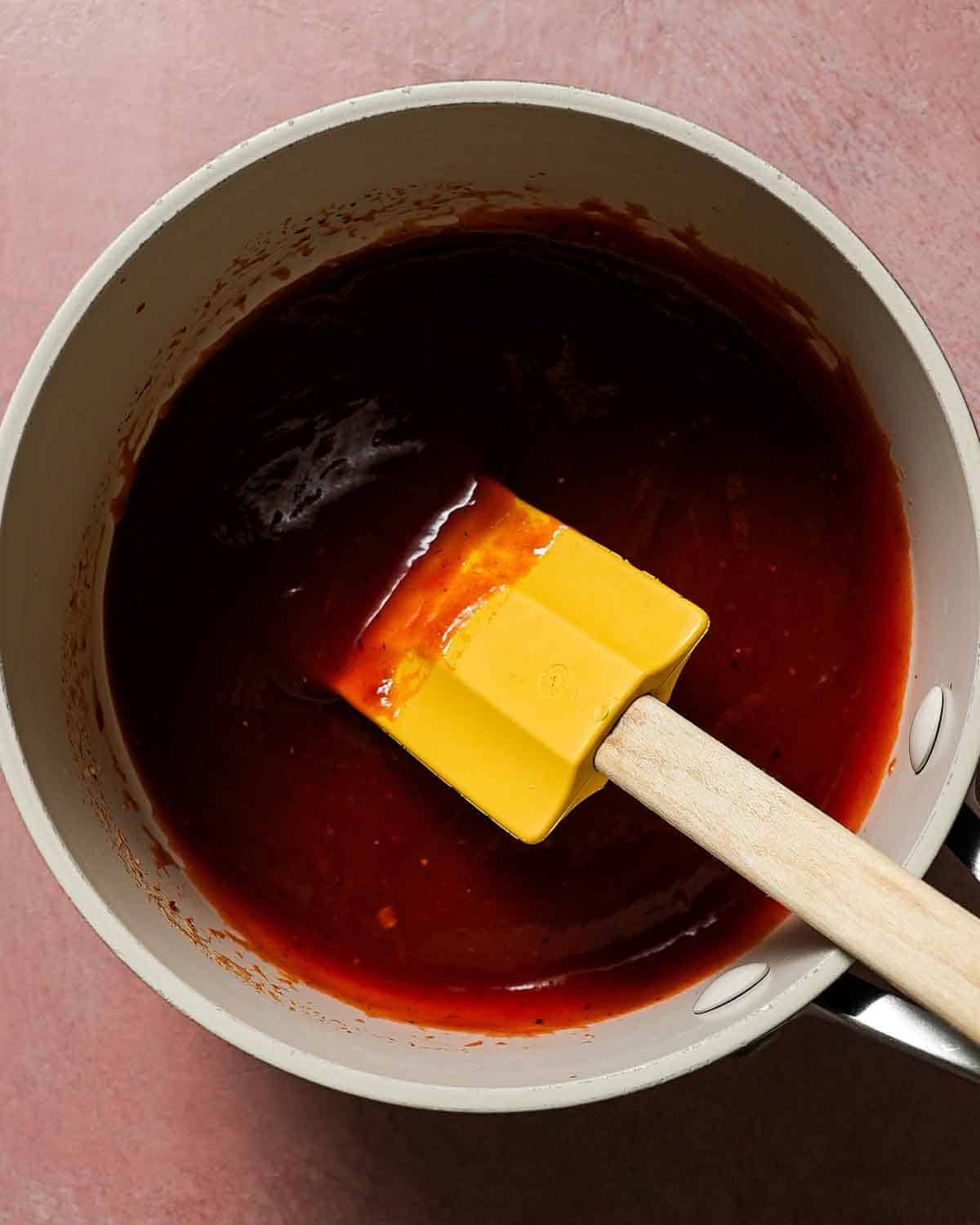 A small pan with chipotle honey bbq sauce with a yellow spatula to stir.