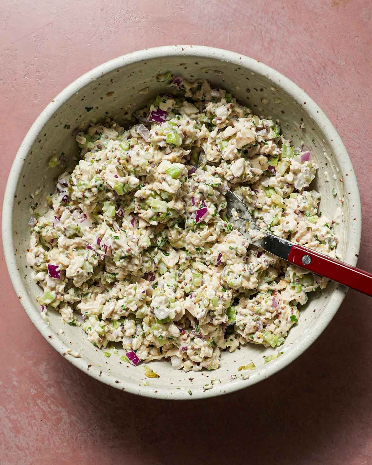 A big bowl of chicken salad with a red spoon in the bowl.