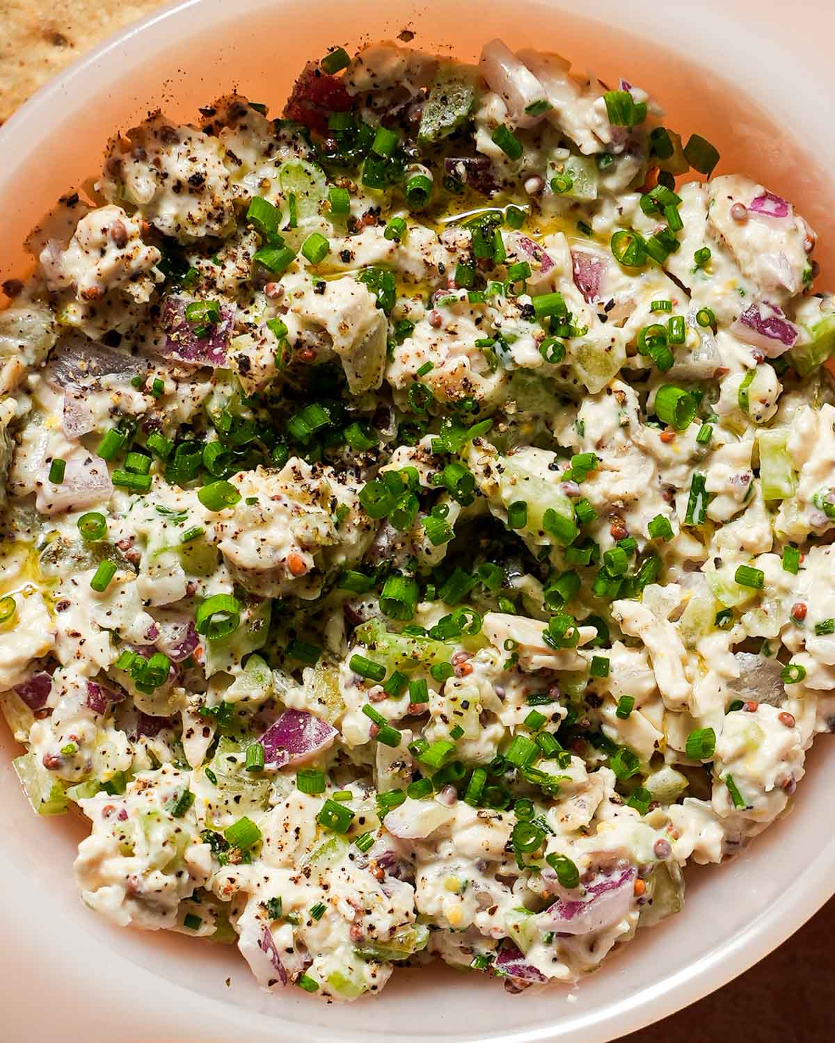 A bowl of chicken salad with chives, red onions and dill pickles.