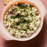 A small bowl of chicken salad with chives, dill pickles with crackers.
