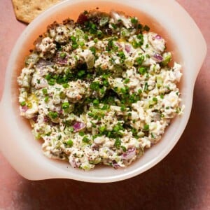 A small bowl of chicken salad with chives, dill pickles with crackers.
