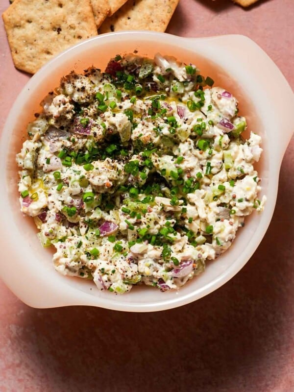 A small bowl of chicken salad with chives, dill pickles with crackers.