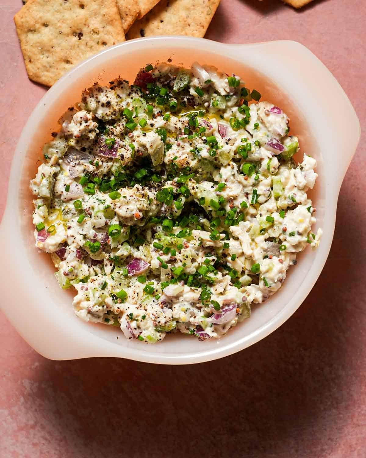 A small bowl of chicken salad with chives, dill pickles with crackers.