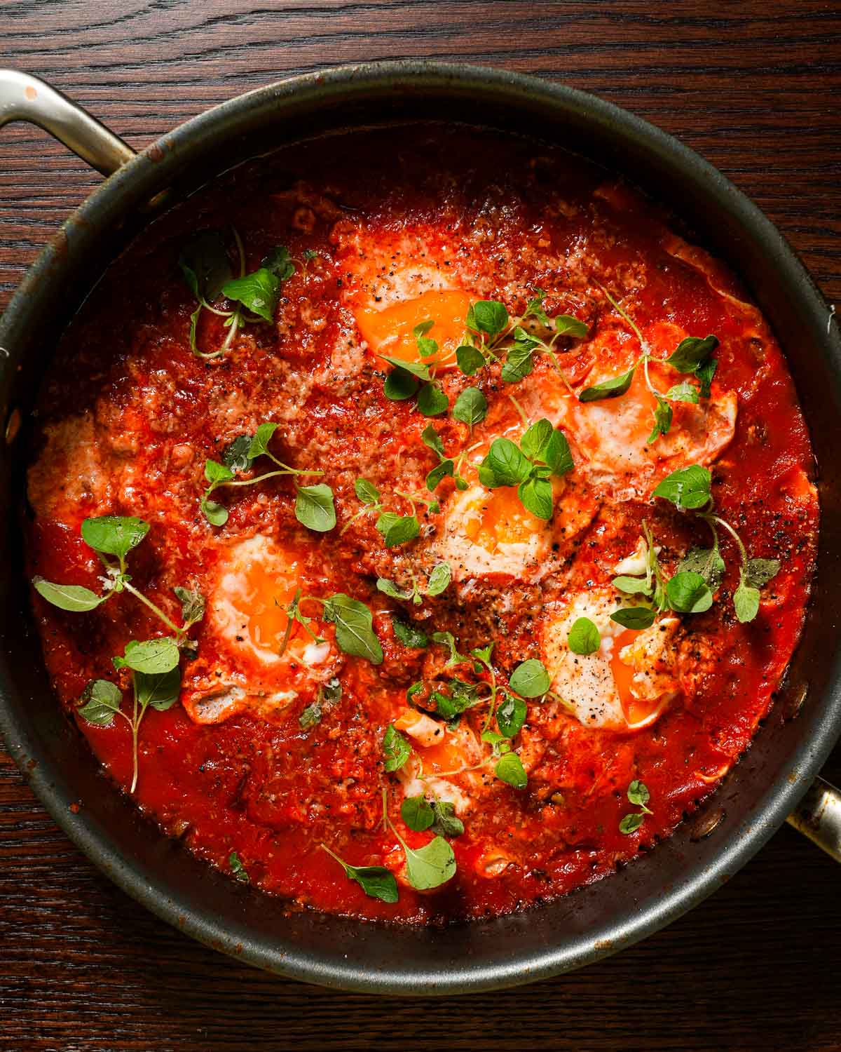 A skillet with spicy tomato sauce stewed with eggs, topped with oregano and parmesan.