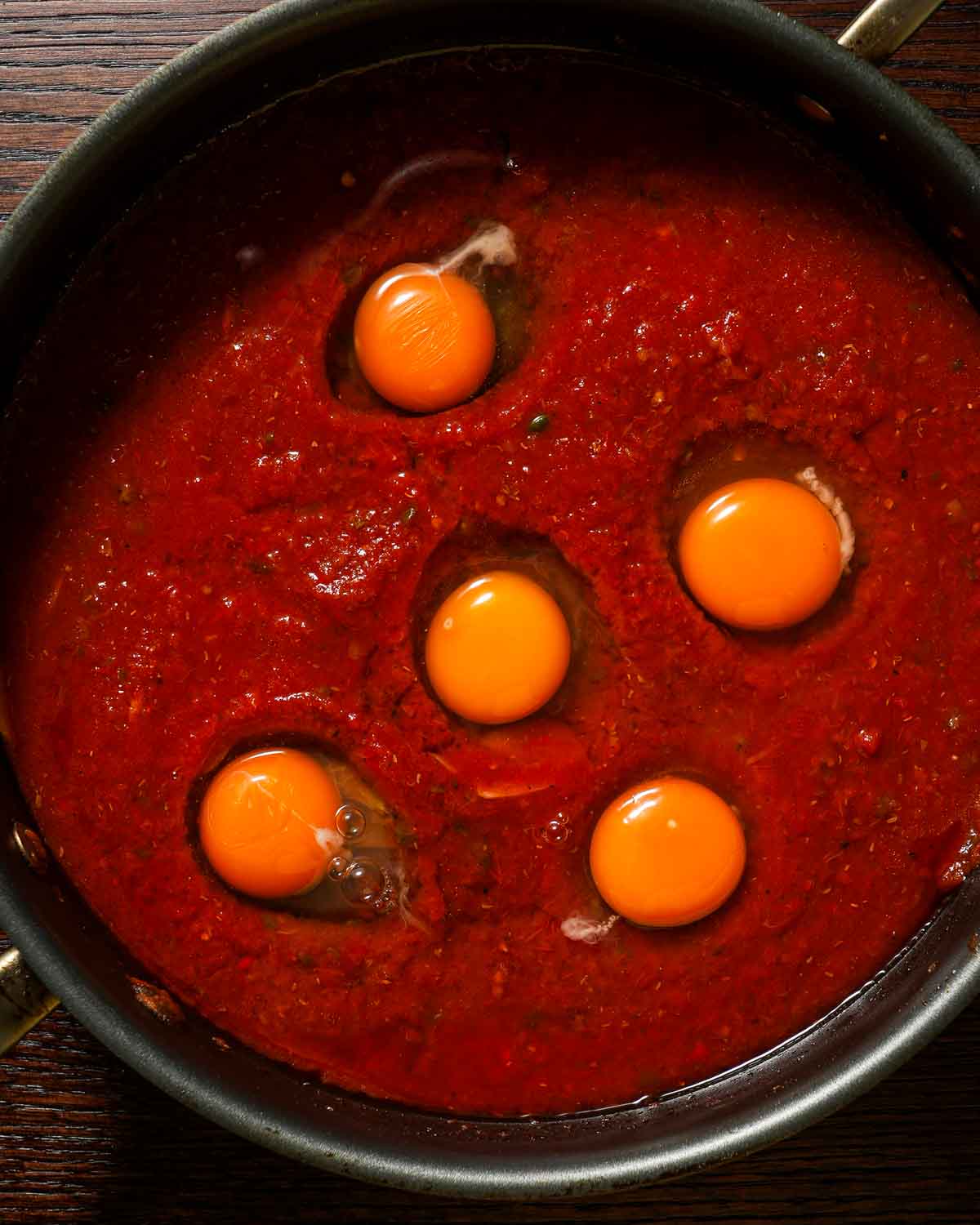 A large skillet with tomato sauce and raw eggs cracked in ready to be poached.