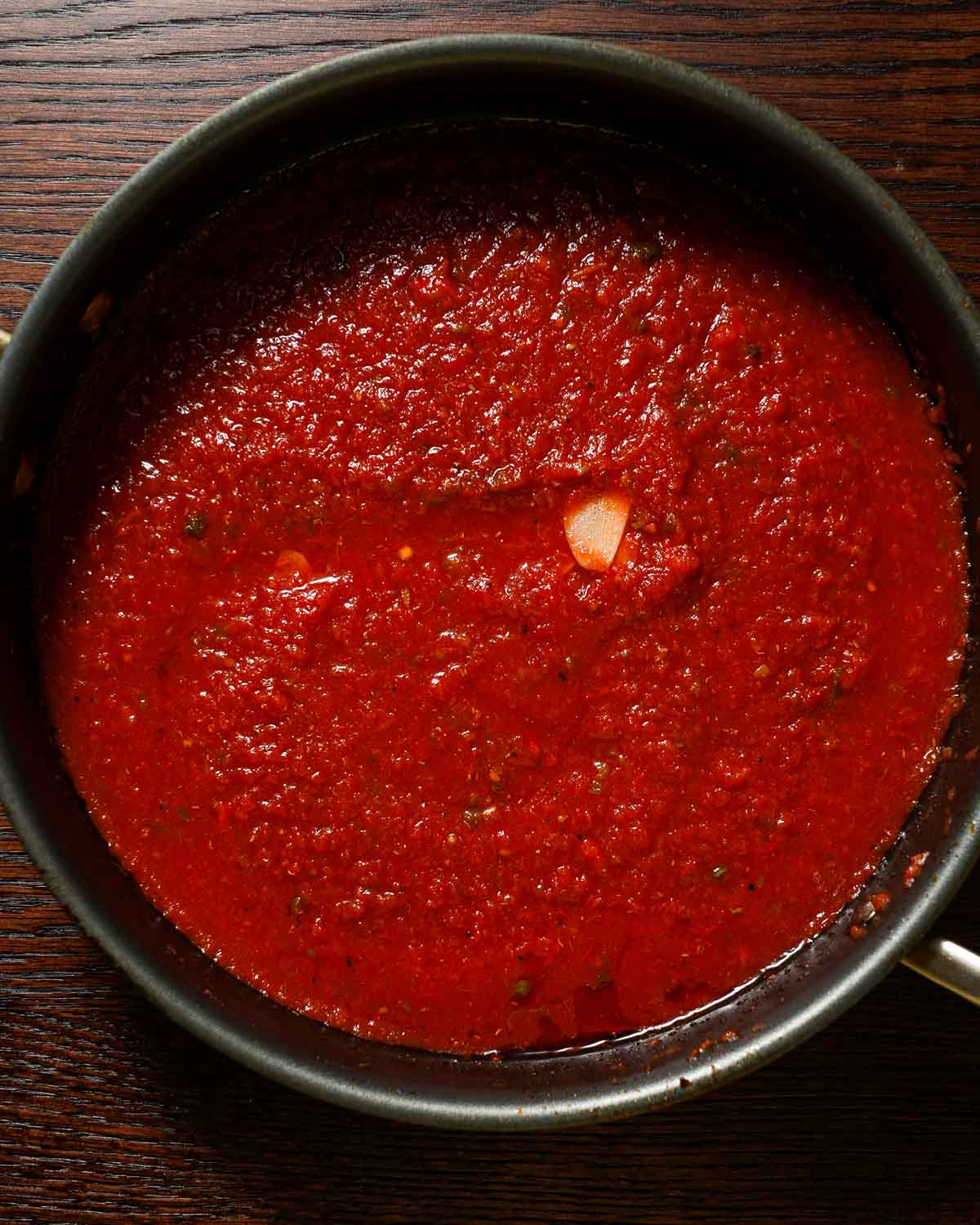 A large skillet with tomato sauce and garlic with capers.