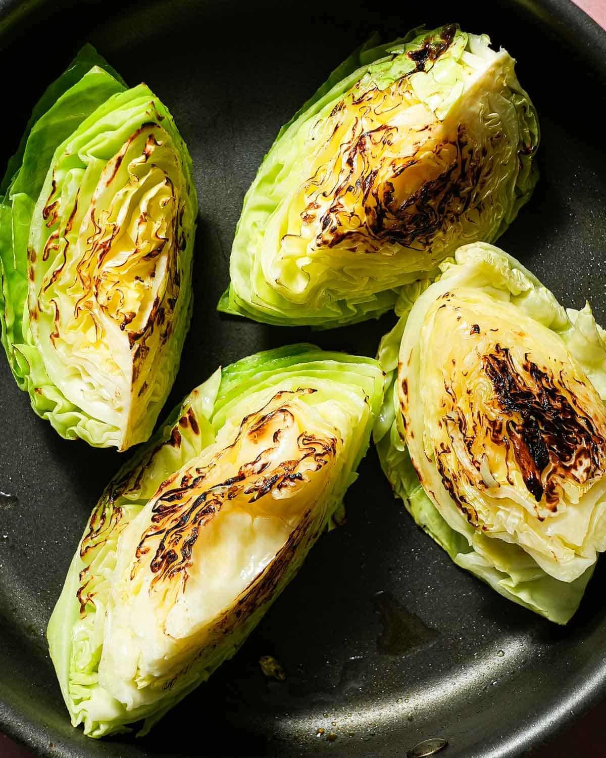 A nonstick skillet with 4 wedges of seared cabbage.