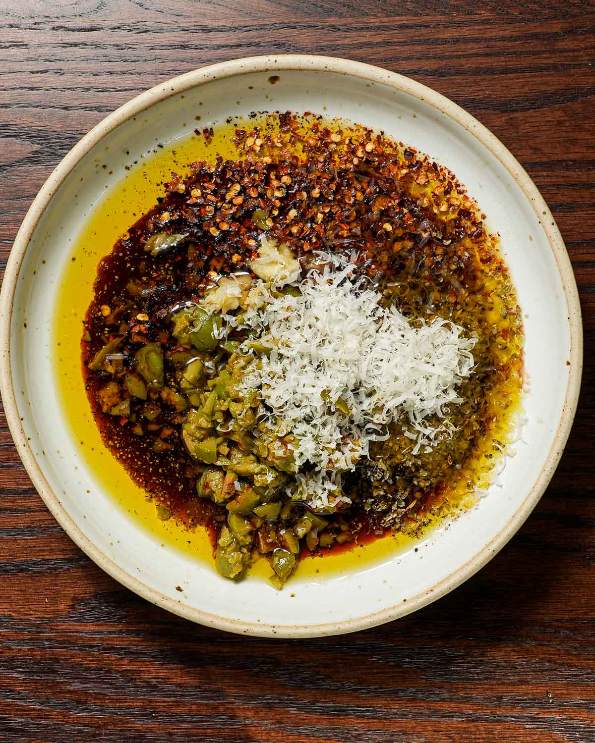 Ingredients in a bowl of bread dipping oil with olives and balsamic vinegar.