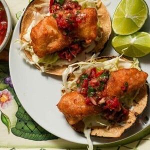 A plate of two crispy fish tacos with a lime wedge with tomato salsa.
