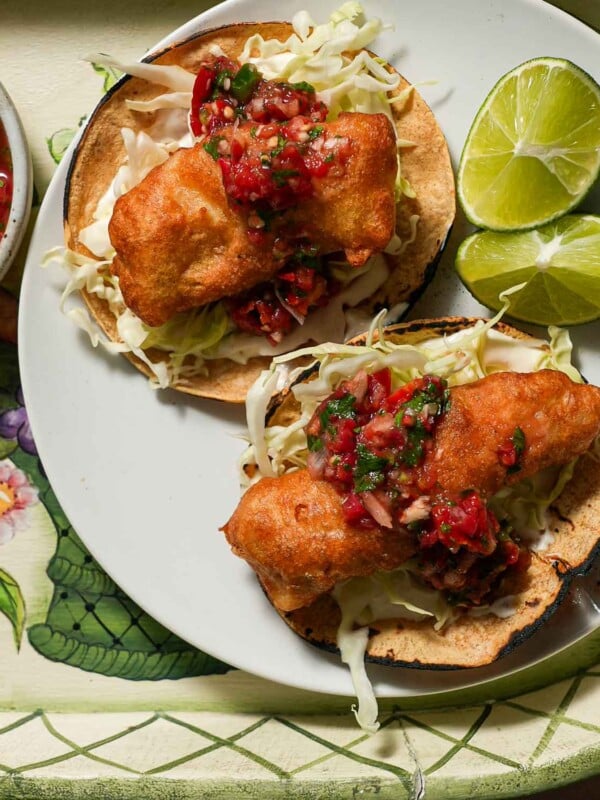 A plate of two crispy fish tacos with a lime wedge with tomato salsa.