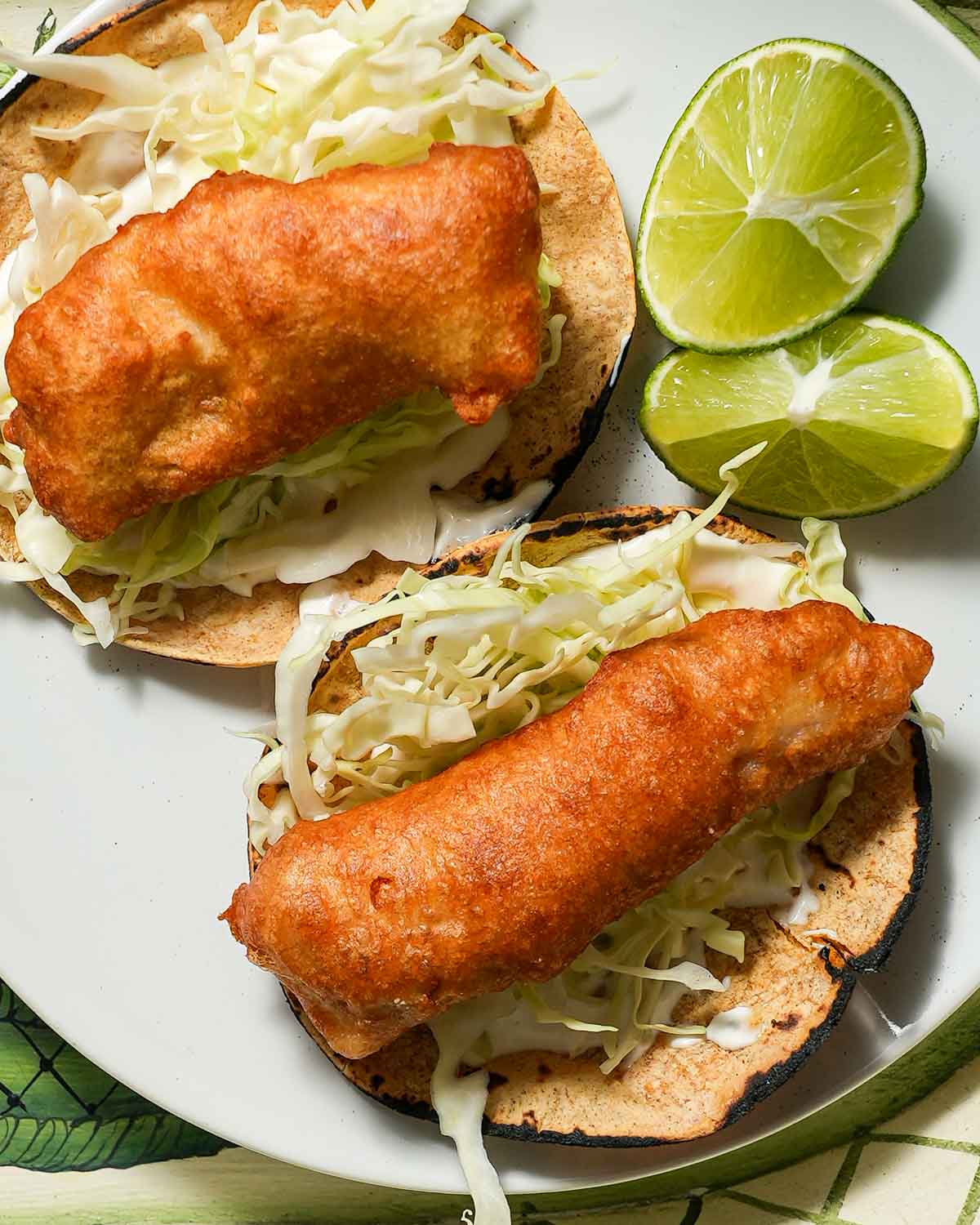 A plate of two crispy fish tacos with a lime wedge.