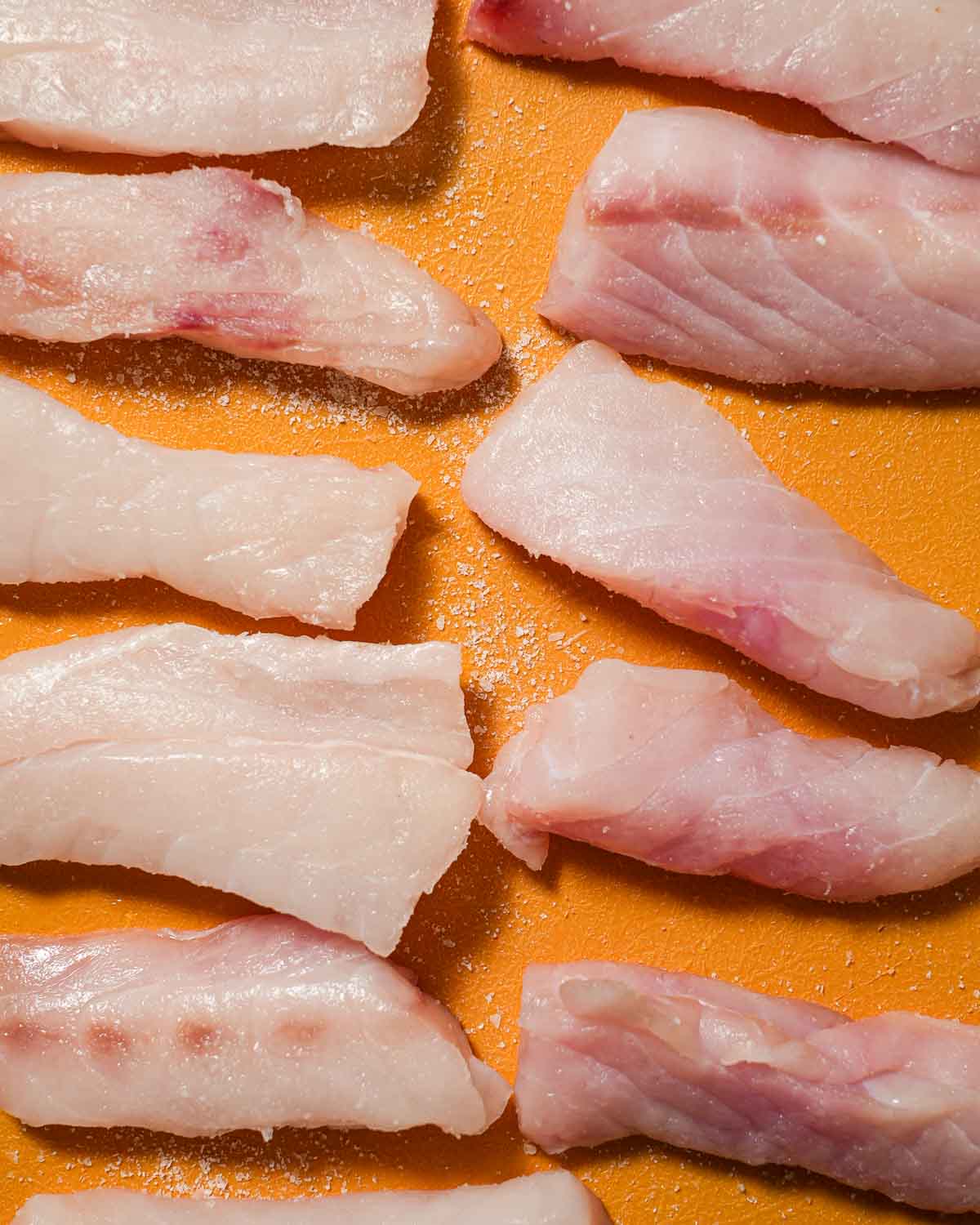 Raw fish being salted on a yellow cutting board.