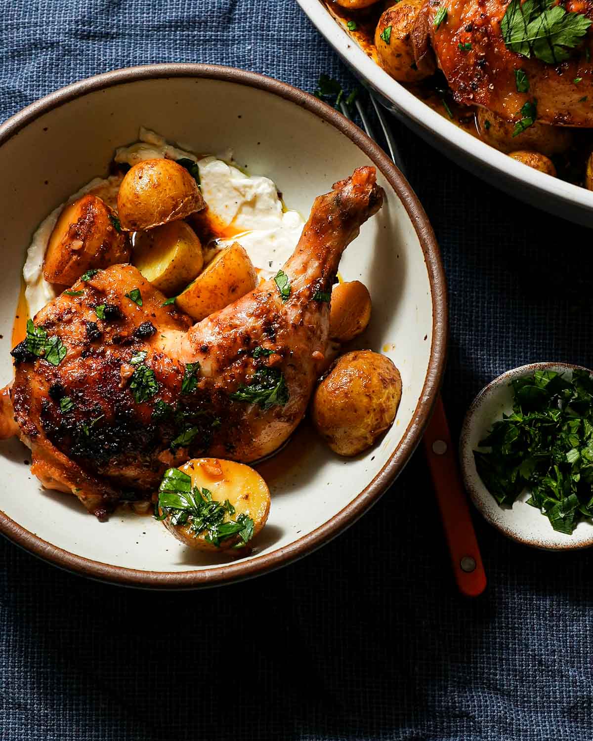 A shallow bowl of greek lemon chicken and potatoes with greek yogurt and parsley.