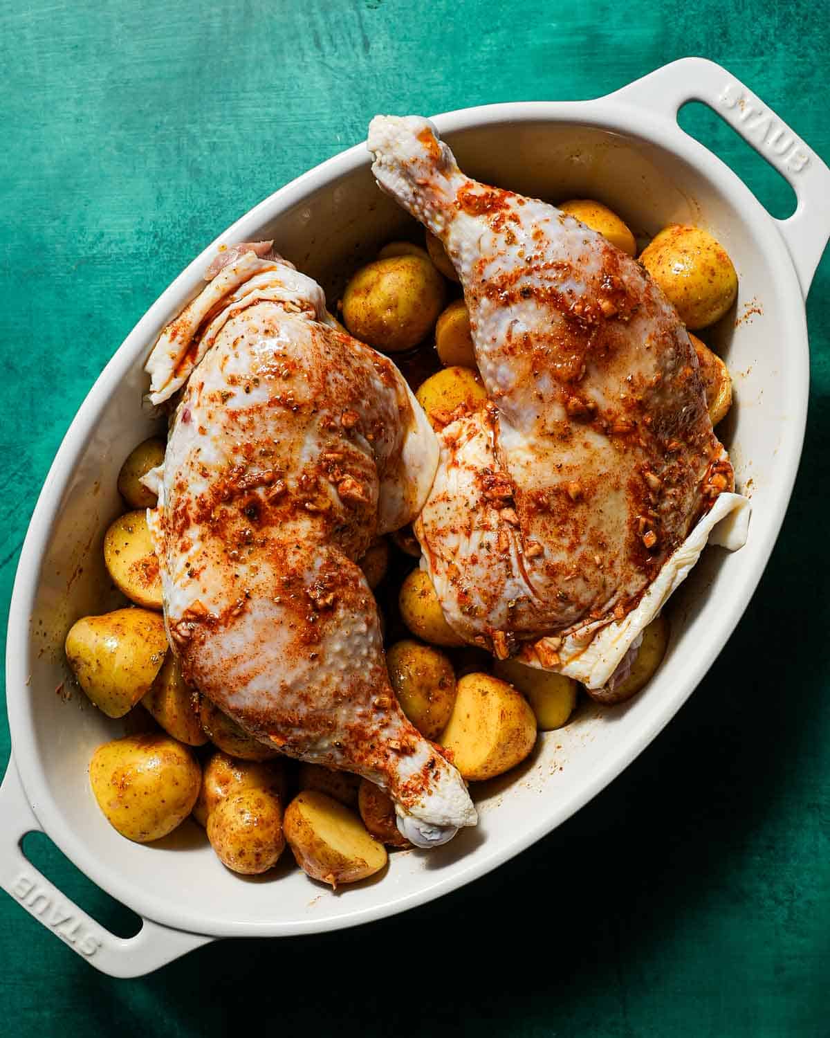 A baking dish of potatoes and 2 chicken legs with spices.