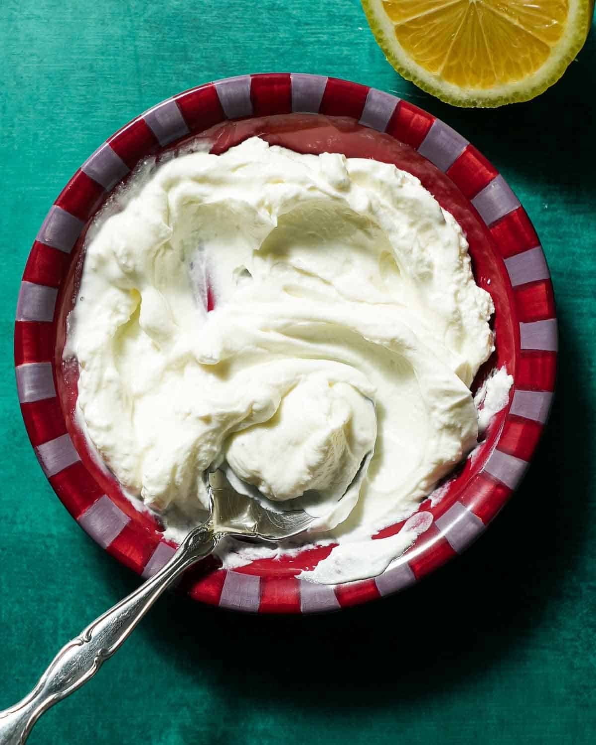 A bowl of yogurt with a spoon being mixed alongside half a lemon.
