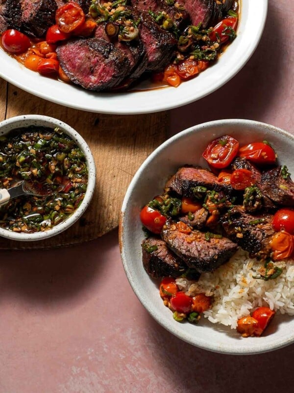 A platter of steak and tomatoes alongside ginger scallion ponzu sauce and a bowl of white rice with steak and tomatoes.