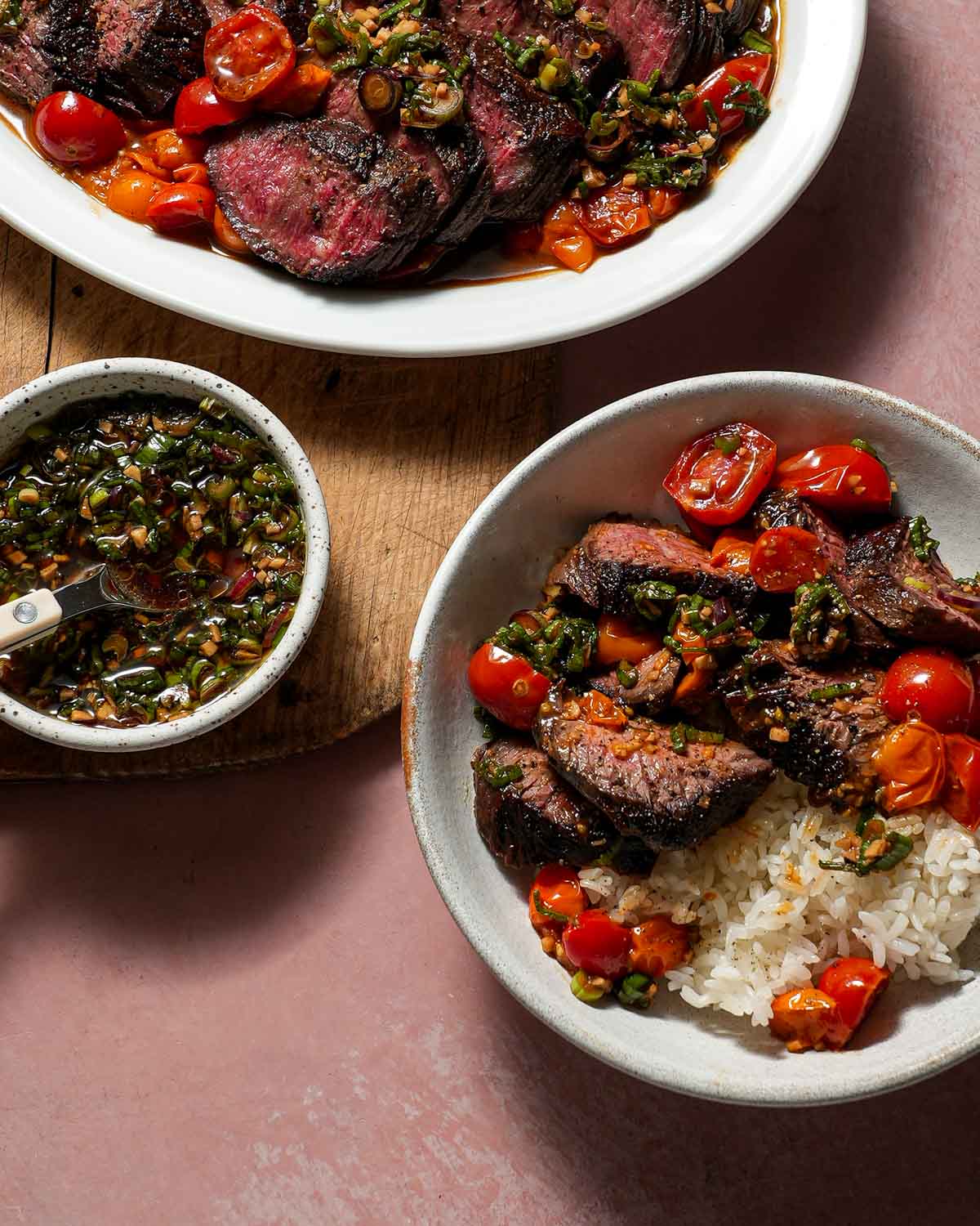 A platter of steak and tomatoes alongside ginger scallion ponzu sauce and a bowl of white rice with steak and tomatoes.