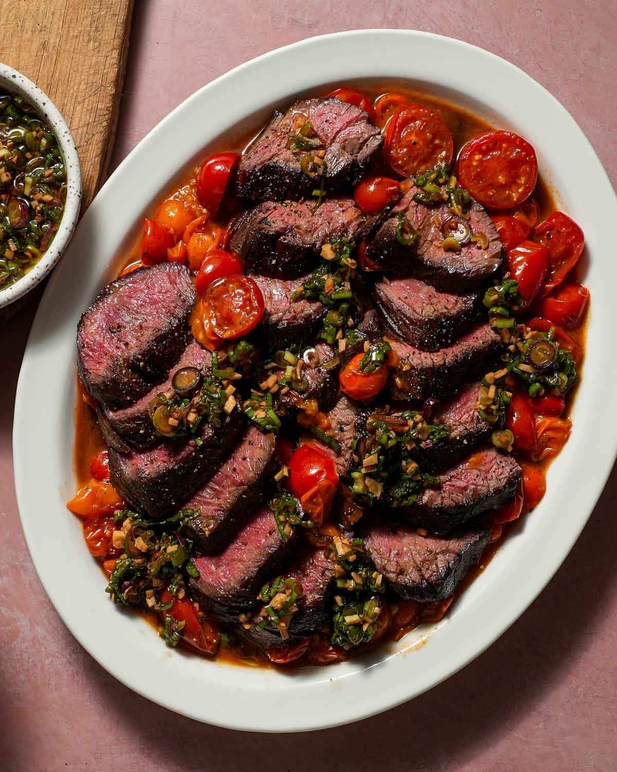 A platter of hanger steak with cherry tomatoes with a ginger scallion ponzu sauce.
