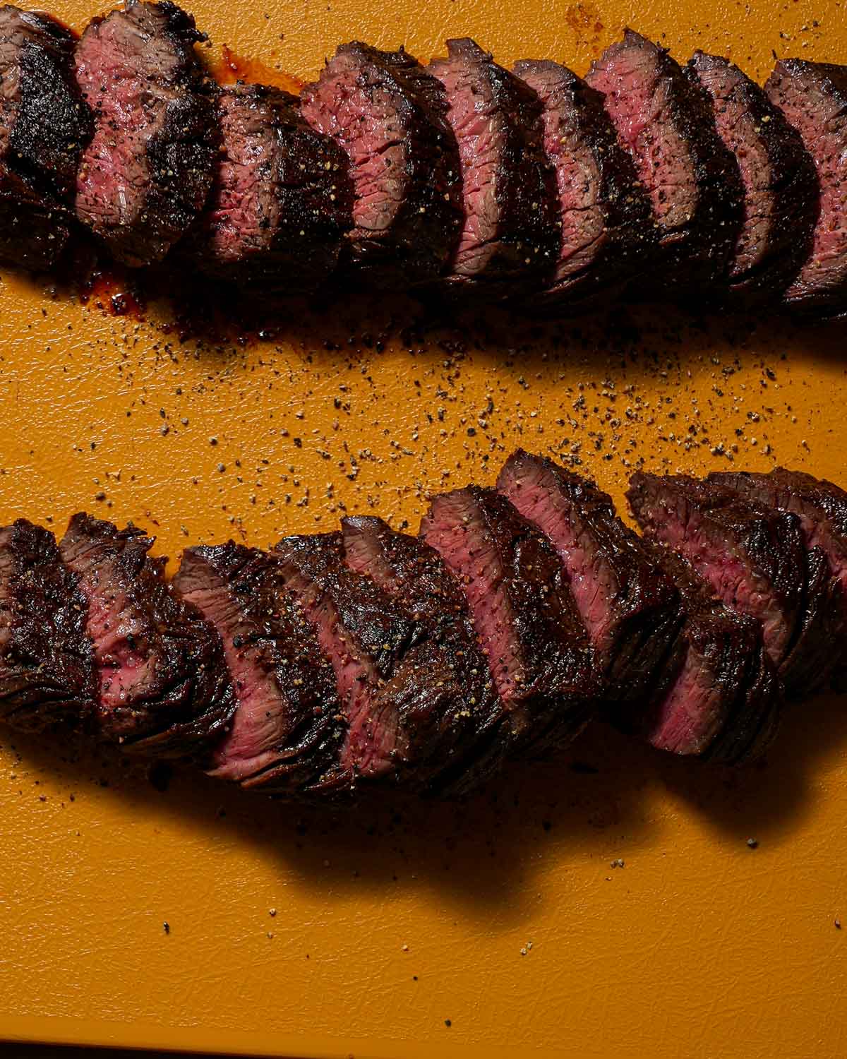 Sliced medium-rare hanger steak with pepper on a yellow cutting board.