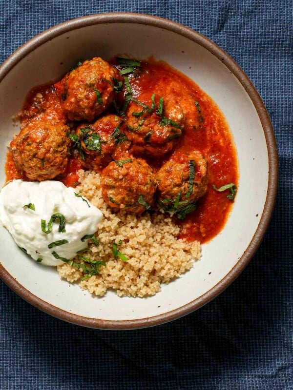 A bowl of lamb meatballs with yogurt, couscous and mint on a blue tablecloth.