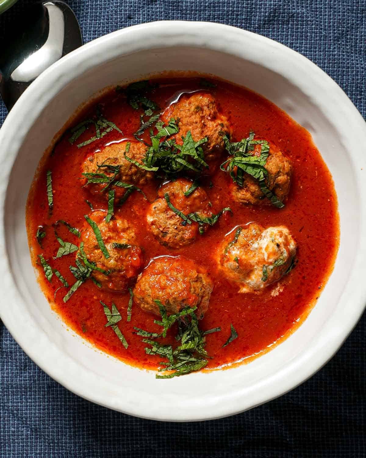 A bowl of lamb meatballs in tomato sauce with sliced mint.