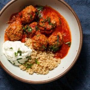 A bowl of lamb meatballs with yogurt, couscous and mint on a blue tablecloth.