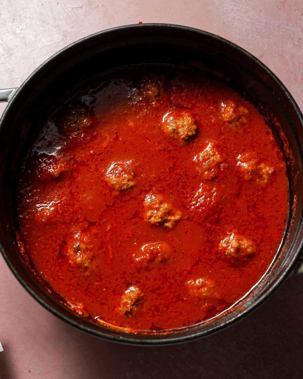 A pot of lamb meatballs being simmered in spicy tomato sauce.