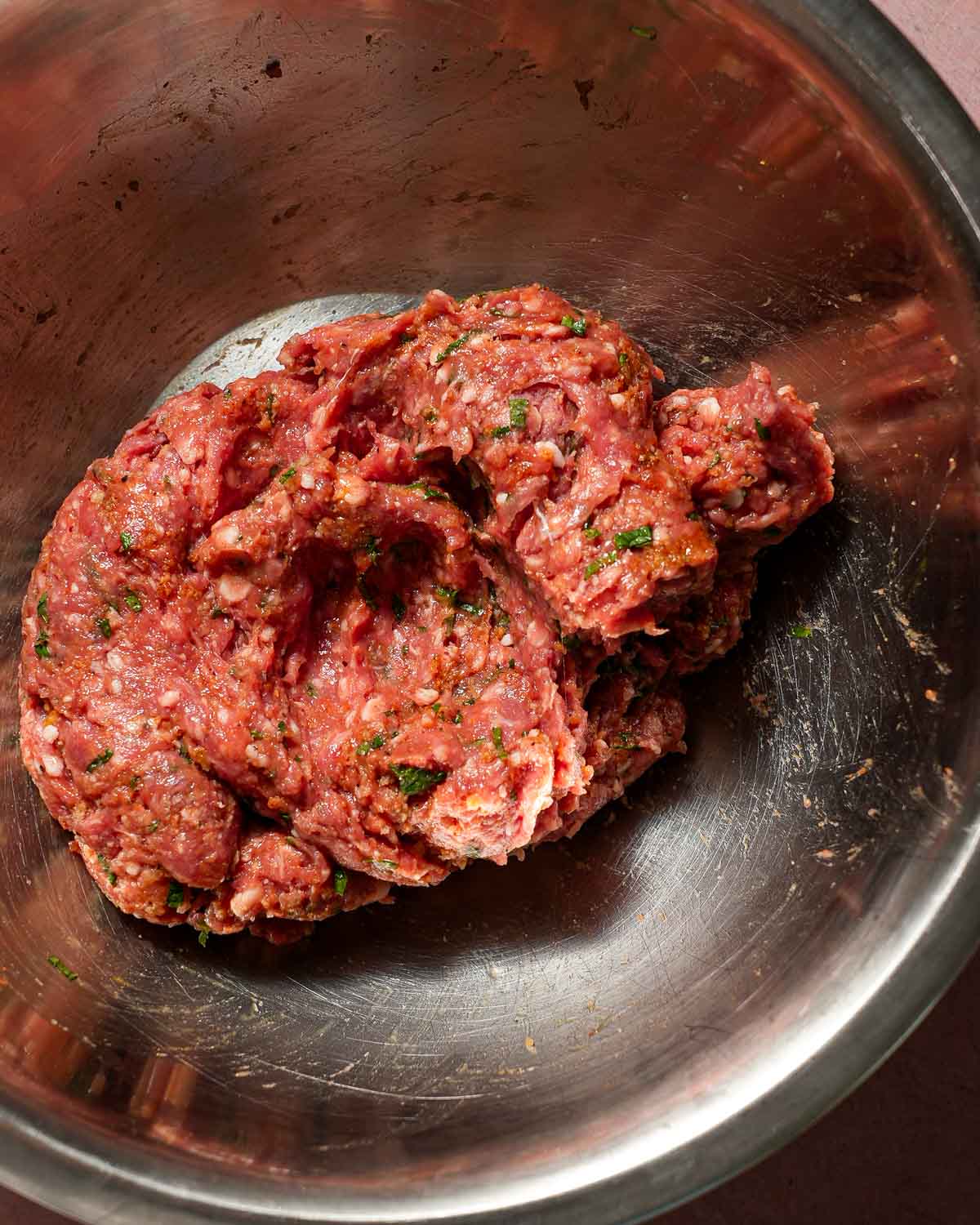 A bowl of ground lamb with spices being mixed together in a large bowl.