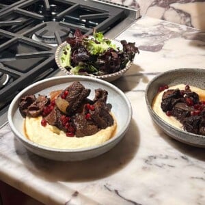 Two plates of pomegranate short ribs with parsnip puree and a salad.