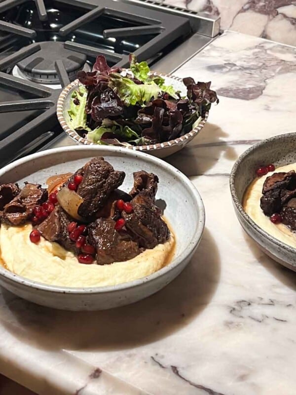 Two plates of pomegranate short ribs with parsnip puree and a salad.
