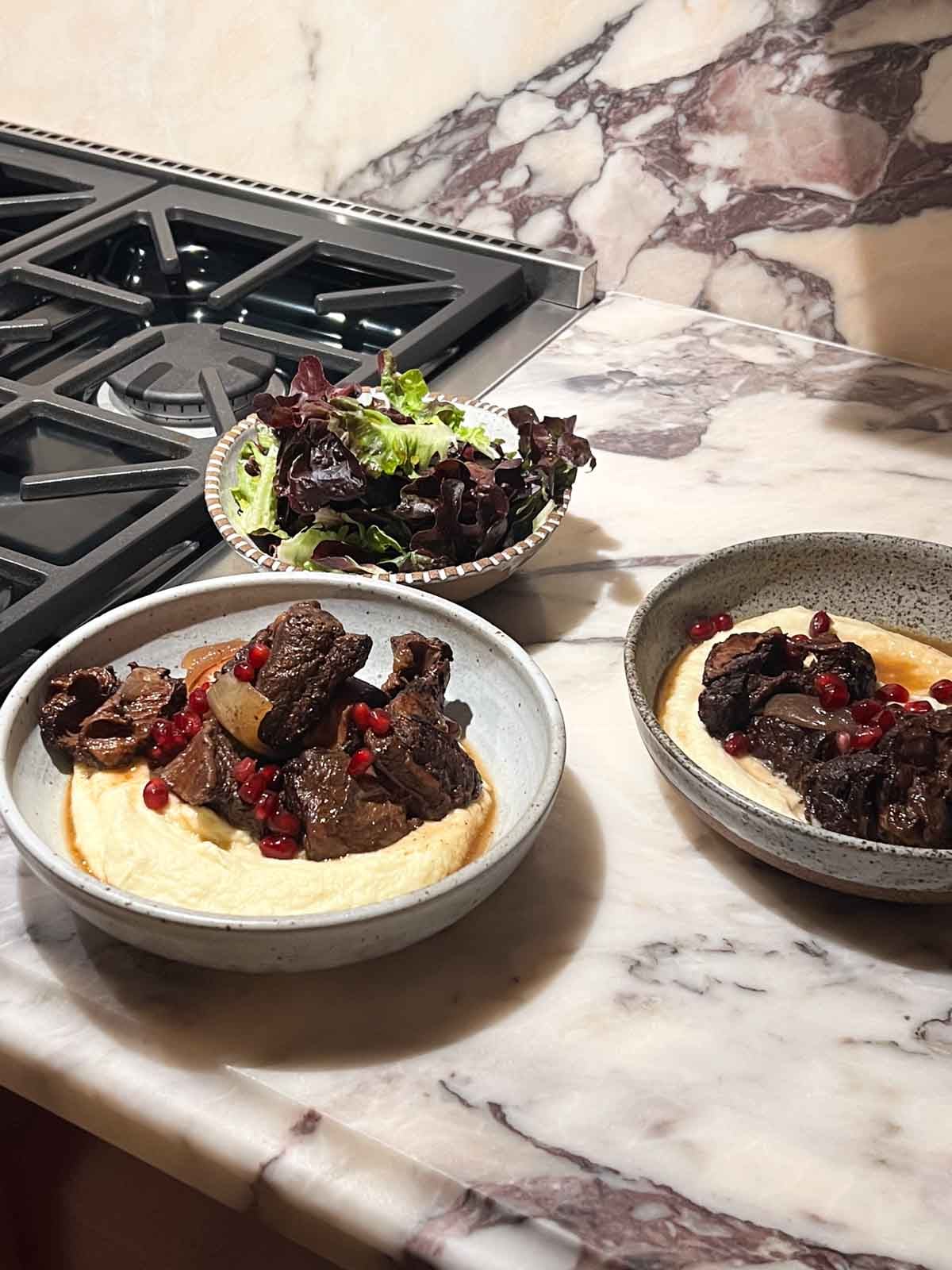 Two plates of pomegranate short ribs with parsnip puree and a salad.