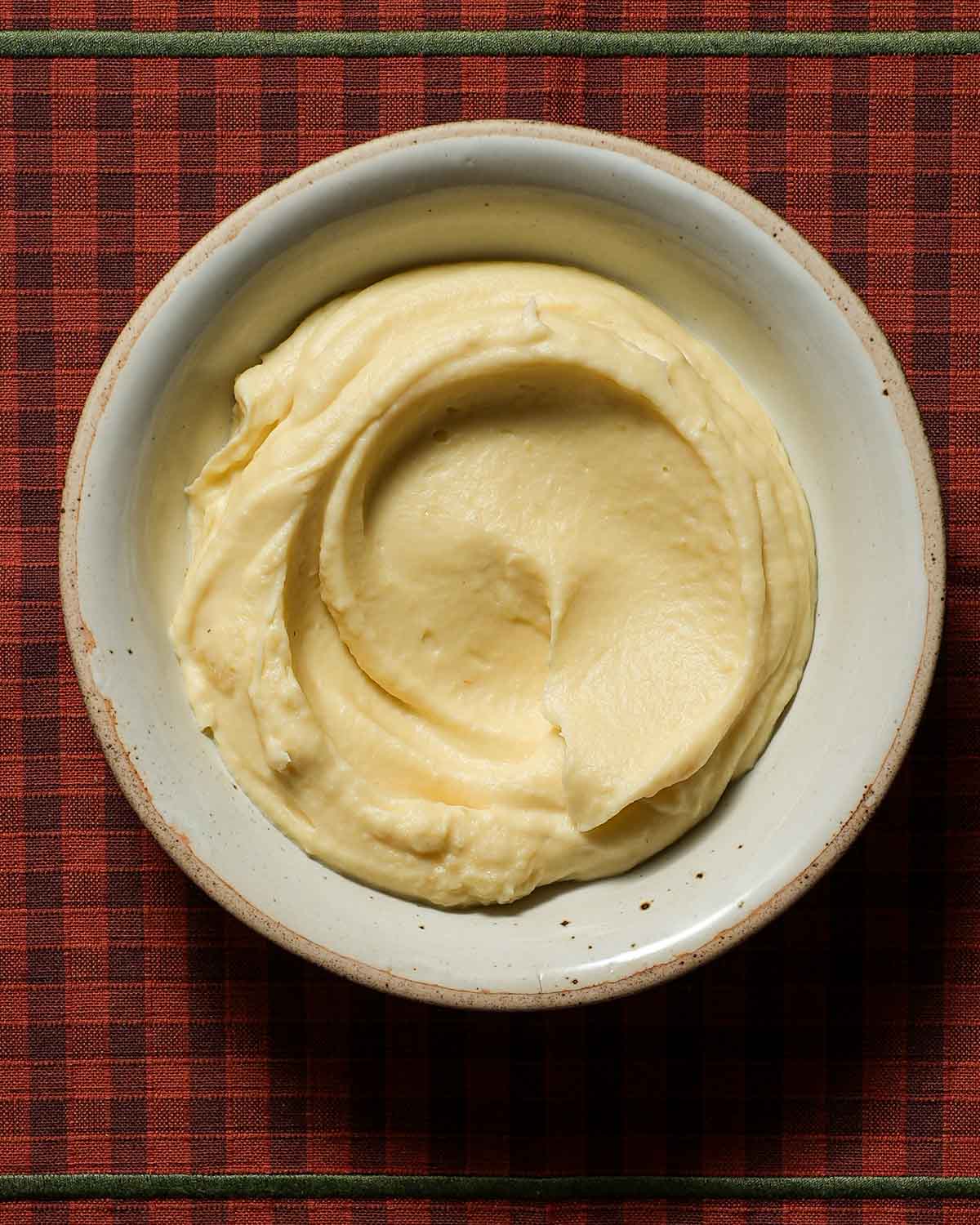 A creamy bowl of parsnip puree on a plaid tablecloth.