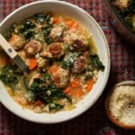 A bowl of Italian wedding soup with a bistro spoon and small bowl parmesan cheese next to it.