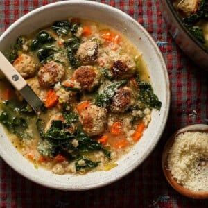 A bowl of Italian wedding soup with a bistro spoon and small bowl parmesan cheese next to it.