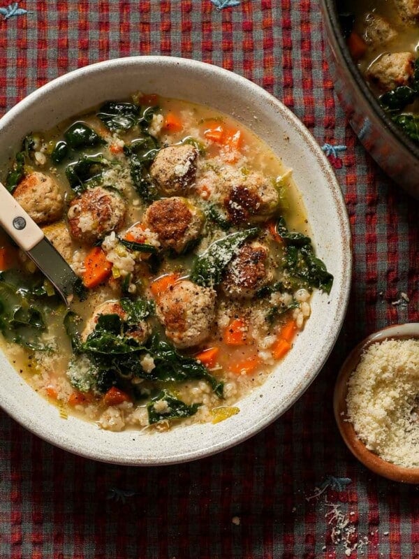 A bowl of Italian wedding soup with a bistro spoon and small bowl parmesan cheese next to it.
