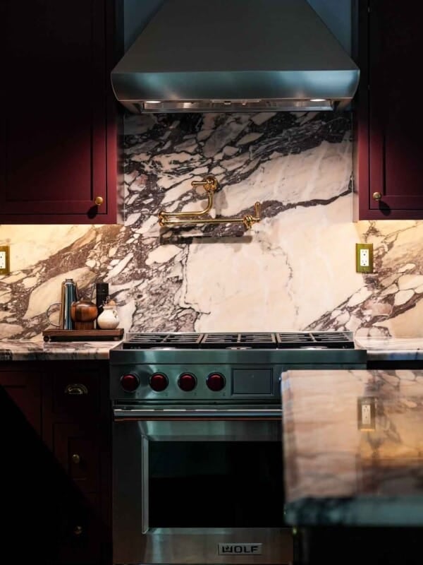 Burgundy kitchen cabiets with arabesco viola marble countertops and blacksplash with a wolf range.