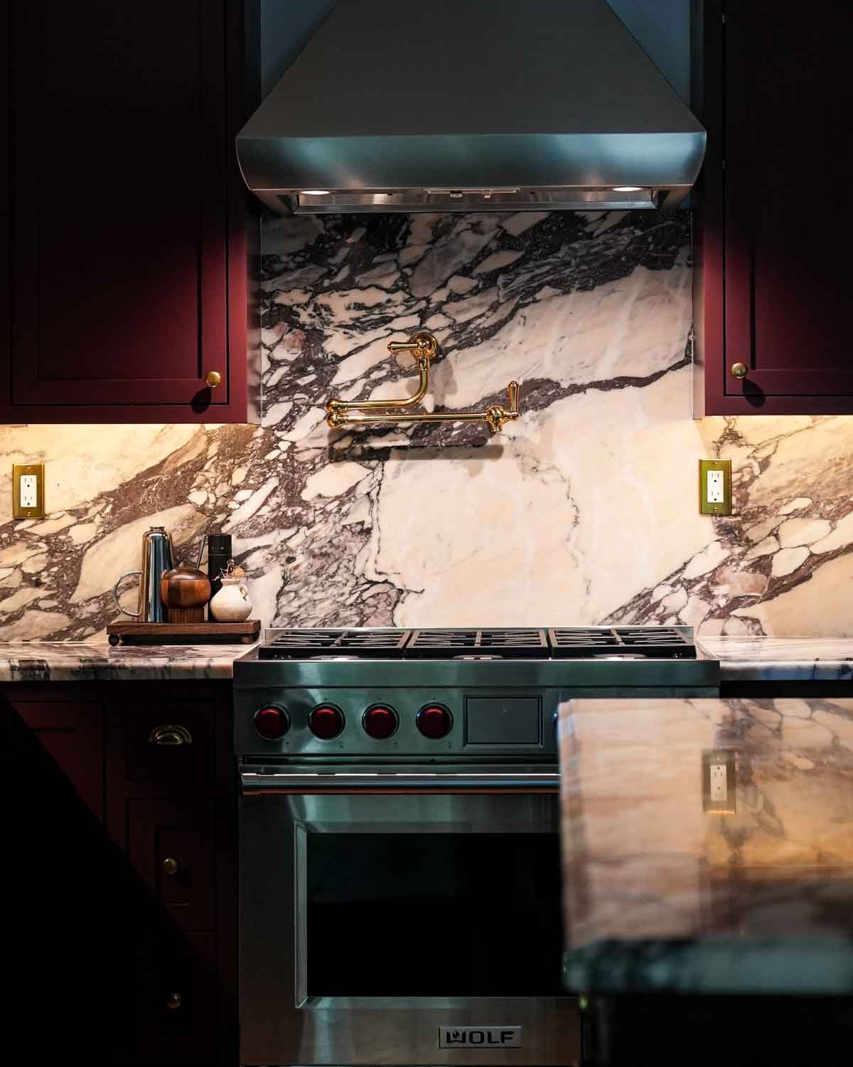 Burgundy kitchen cabiets with arabesco viola marble countertops and blacksplash with a wolf range.