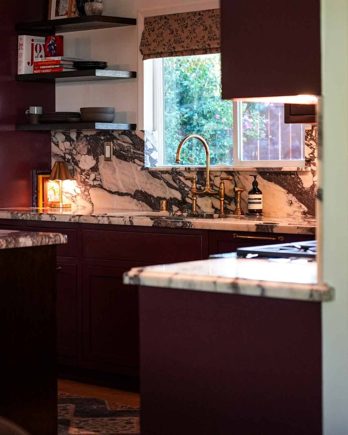 Kitchen remodel that includes burgundy cabinets and marble countertops with brass finishes.