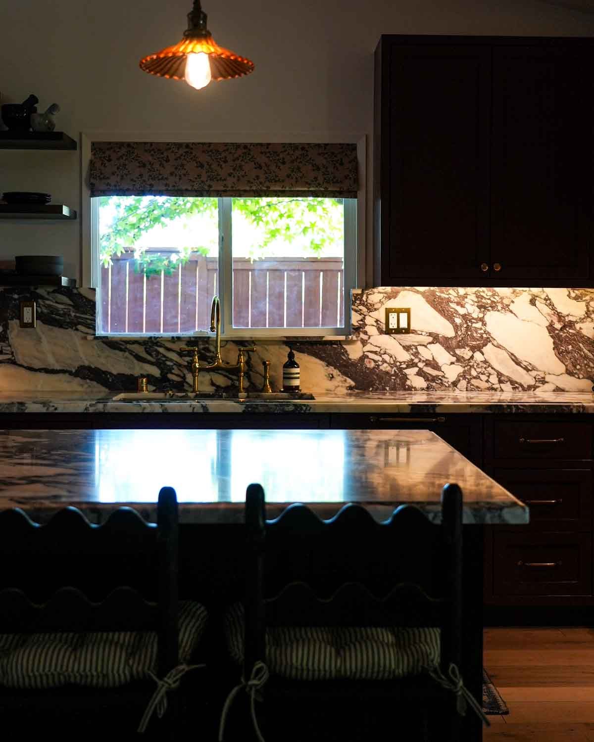 Kitchen renovation in Los Angeles with burgundy cabinets, marble, and a floral window curtain.