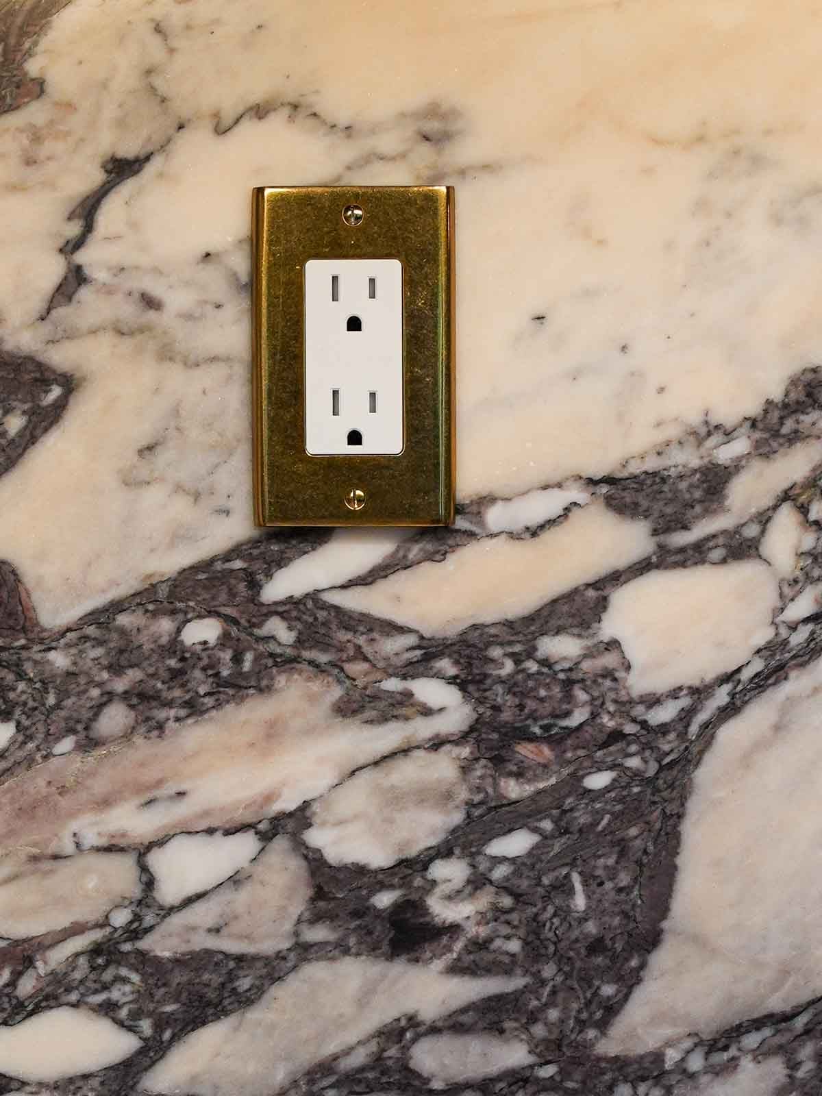 Brass outlet cover with marble in the background of a kitchen renovation.