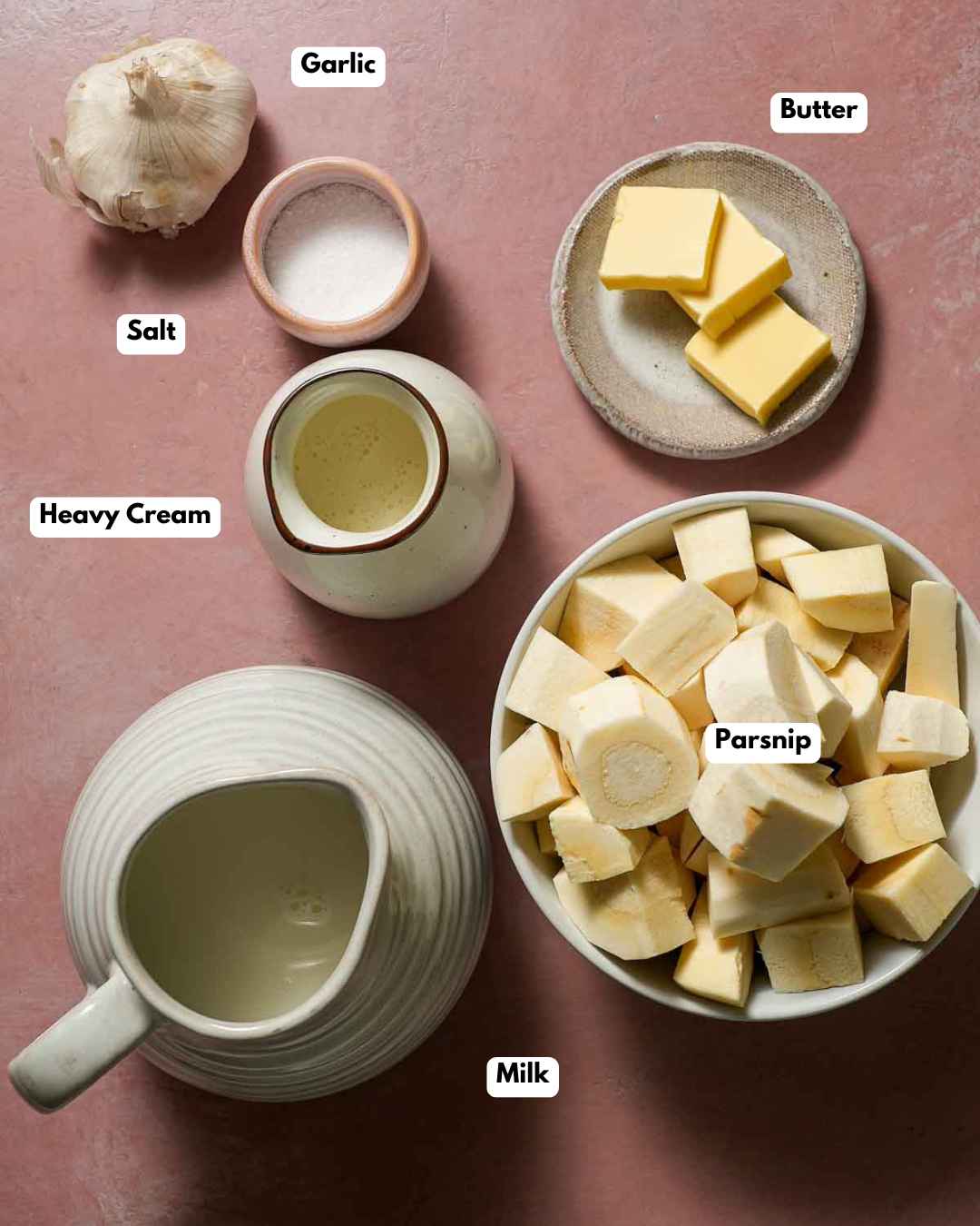 The ingredients laid out to make a garlic parsnip puree on a pink table.