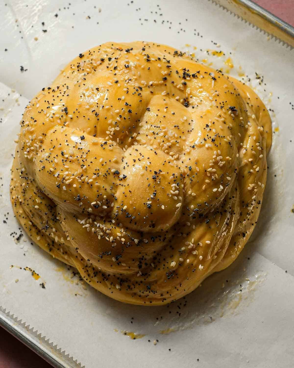Braided challah topped with egg wash and seeds ready to be baked.