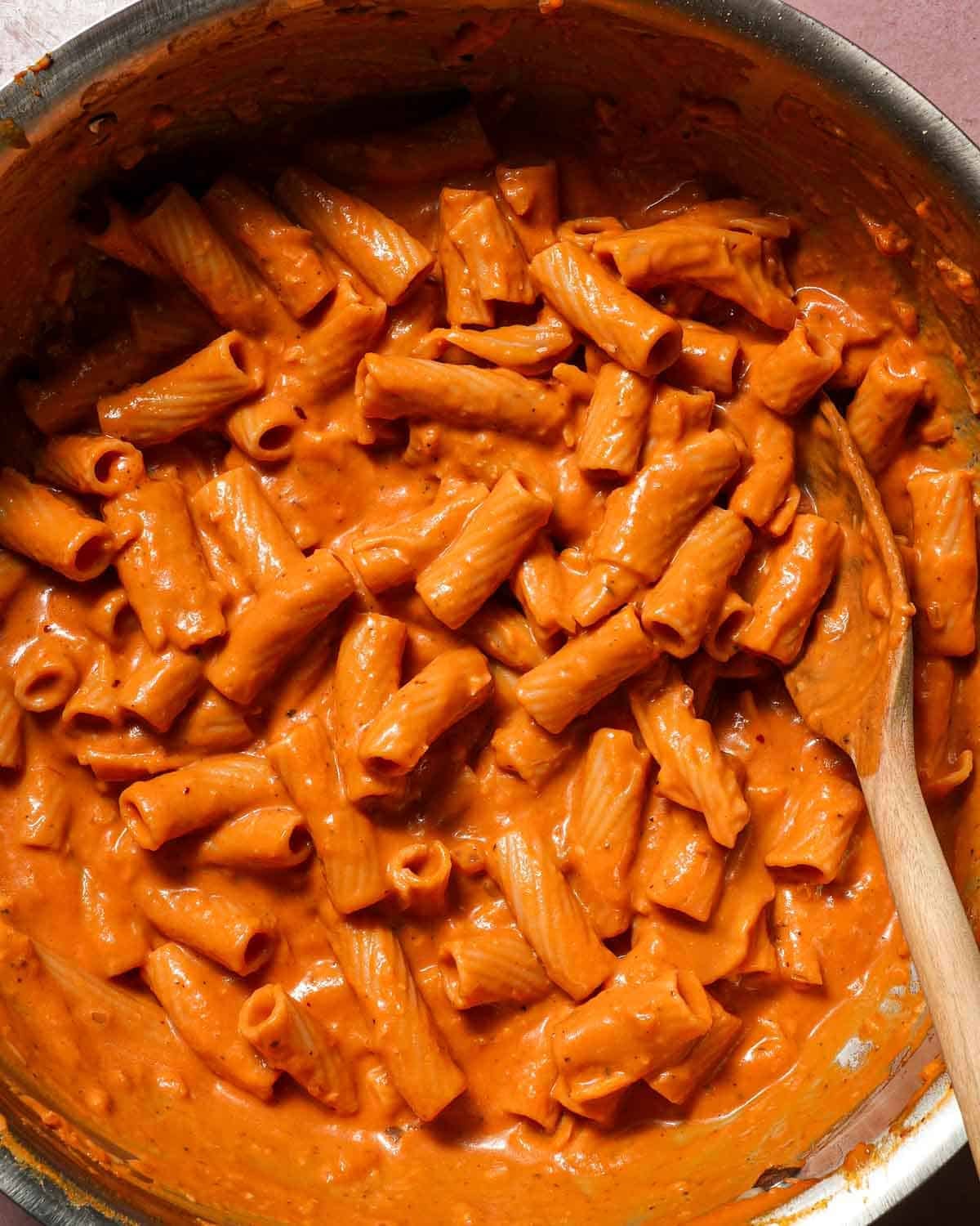 A pot of pumpkin rigatoni being stirred with a wooden spoon.