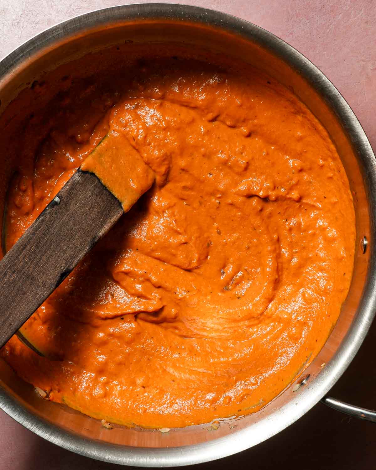 A pot of pumpkin rigatoni sauce being stirred.